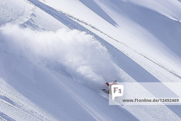 Ein weiblicher Snowboarder macht einen Powder Turn und sprüht eine Wolke Schnee in die Luft an einem sonnigen Tag am Cerro Catedral in Argentinien