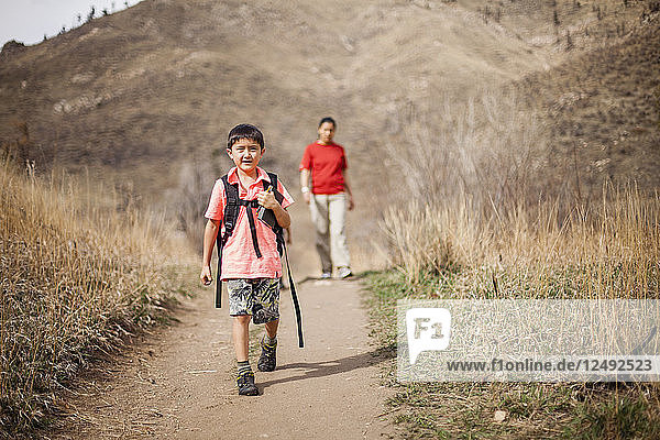 A 6 year old Japanese American boy hikes with his mother in the background on the Hewlett Gulch Trail  Colorado.