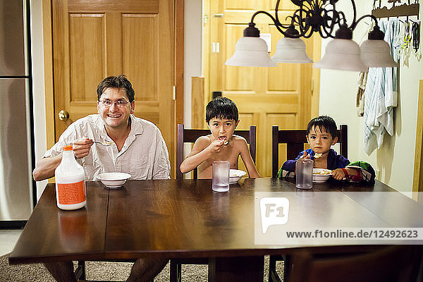 A dad and his seven-year-old and four-year-old sons eat cereal at a table while on vacation.