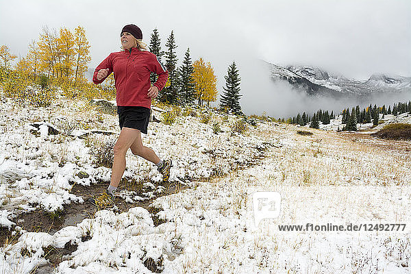 A woman trail running through a fall snowstorm and yellow aspens on Molas Pass in the San Juan National Forest  Silverton  Colorado.
