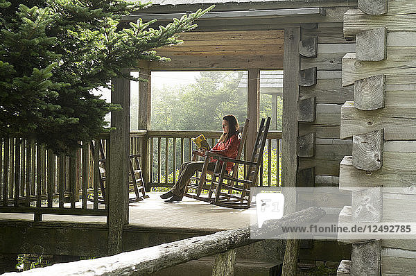 Eine Frau in einem Schaukelstuhl liest auf der Veranda einer Hütte der Leconte Lodge  Mount Leconte  Great Smoky Mountain National Park  Gatlinburg  Tennessee.