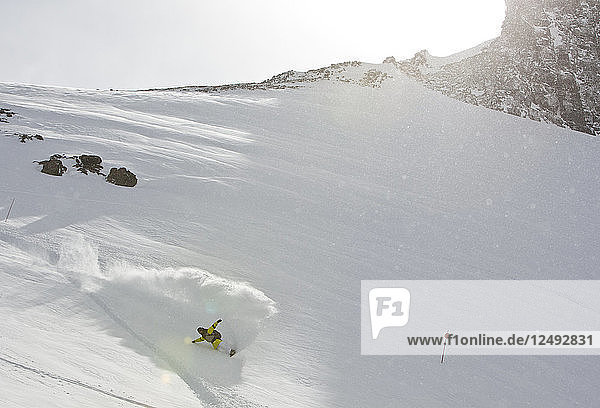 Ein Snowboarder macht einen Powder Turn und spritzt Schnee hoch in die Luft am Cerro Catedral