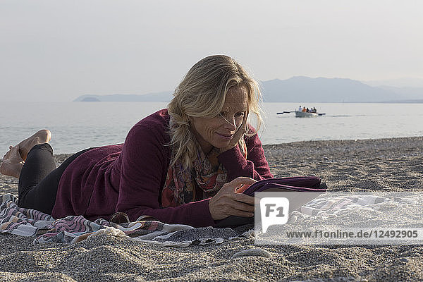 Frau lehnt sich am Strand zurück und benutzt digitales Tablet