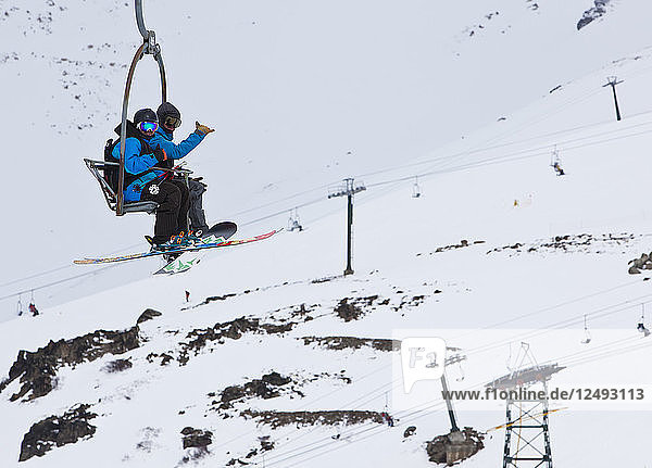 Ein Skifahrer und ein Snowboarder fahren gemeinsam auf einem Sessellift am Cerro Catedral in Argentinien