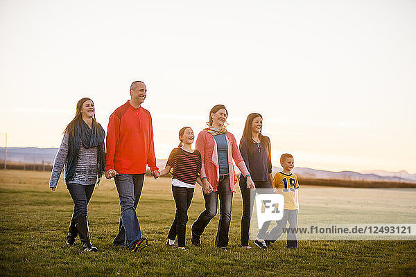 Eine Familie Spaziergang durch ein Feld bei Sonnenuntergang  während die Hände in Bozeman  Montana