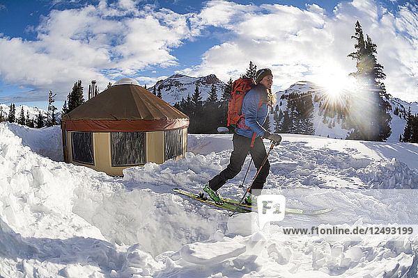A woman backcountry skiing away from a yurt after camping on Red Mountain Pass  Silverton  Colorado.