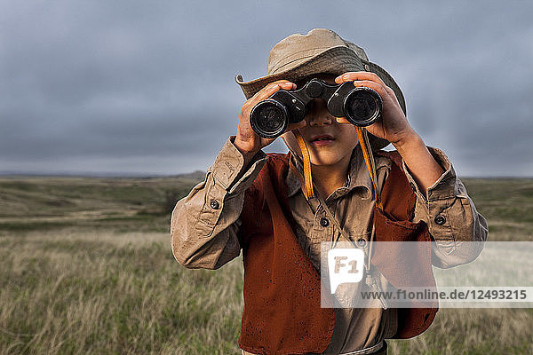 A 6 year old Japanese American boy dressed as an explorer with a hat and vest surveys the land (grasslands and prairies) with his binoculars in Badlands National Park  South Dakota.