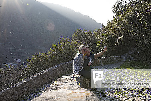 Paar sitzt auf Steinmauer und macht Selfie