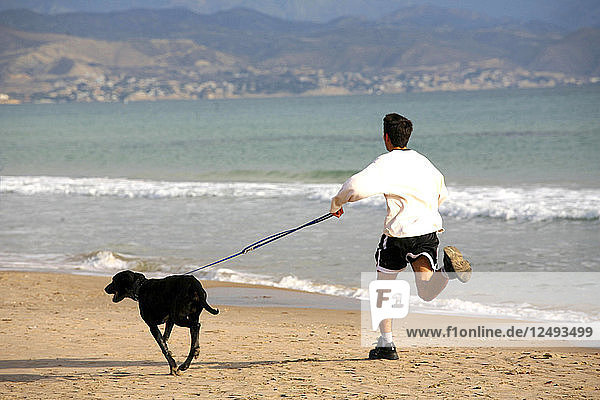 A young boy and dog run along a quiet beach in Aliicante