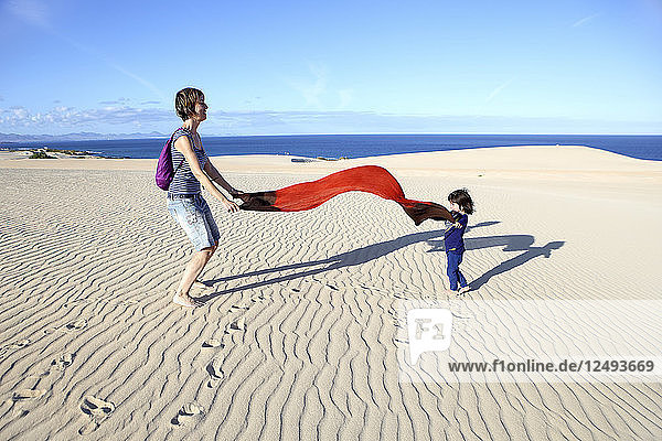 Mother And Daughter Spreading Red Cloth In Dunes Of Corralejo  Spain