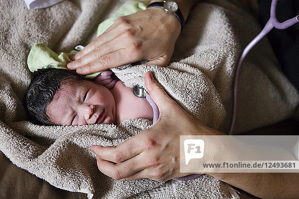 Hebamme überprüft die Herzfrequenz eines neugeborenen Babys mit Stethoskop