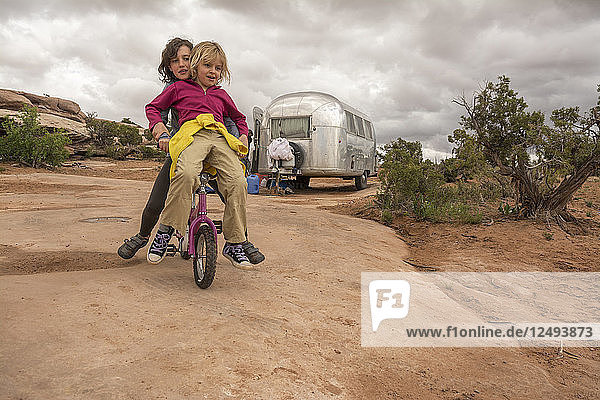 Two girls playing on a tiny mountain bike while camping near Dead Horse State Park  Moab  Utah.