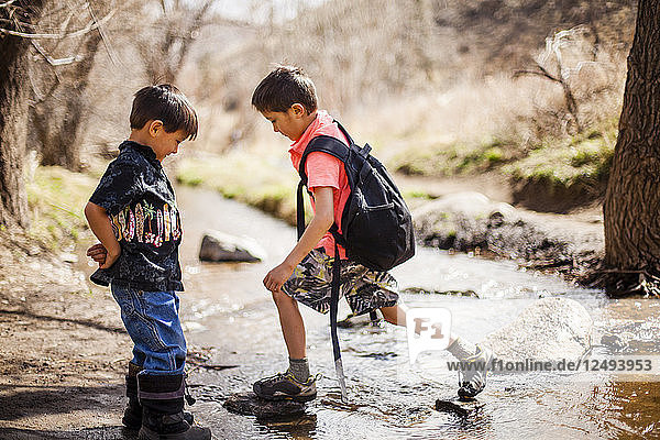A four year old and 6 year old Japanese American boys cross a stream while hiking along the Hewlett Gulch Trail  Colorado.