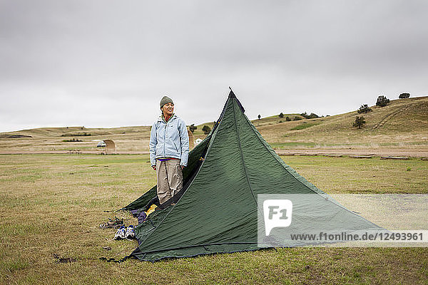 Eine japanische Amerikanerin steht nach einer Regennacht in ihrem Zelt und begutachtet das Land auf dem primitiven Campingplatz  Sage Creek Campground  Badlands National Park  South Dakota.
