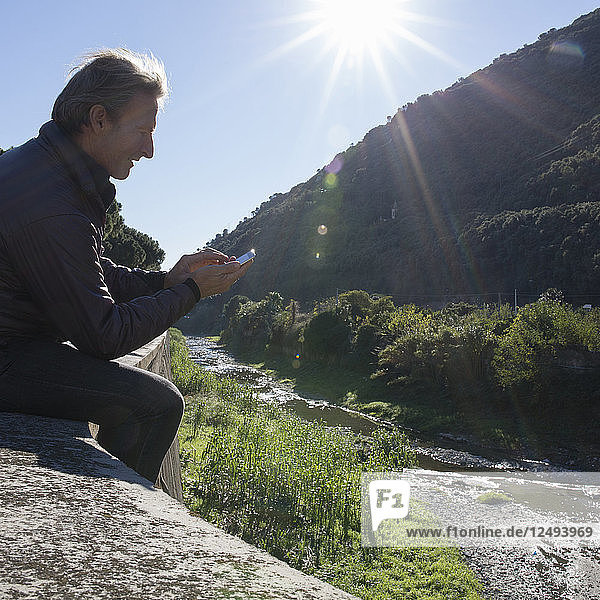 Mann benutzt digitales Telefon auf Felsvorsprung über Fluss