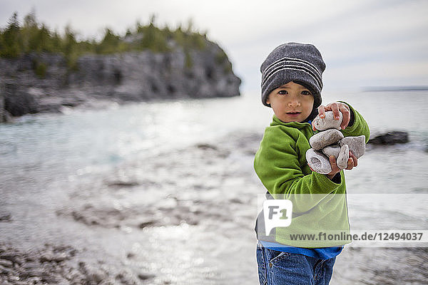 A 4 year old Japanese American boy holds a stack of rocks on the shore of Lake Huron  while exploring The Grotto of the Bruce Peninsula National Park  Ontario  Canada.