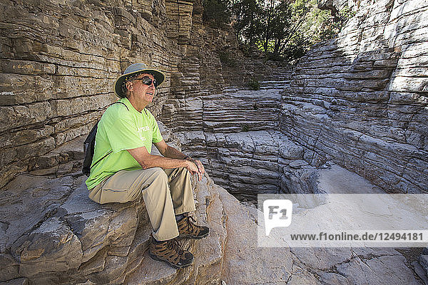 Lächelnder älterer Mann  der eine schmale trockene Schlucht mit steilen  geschichteten Felswänden erkundet