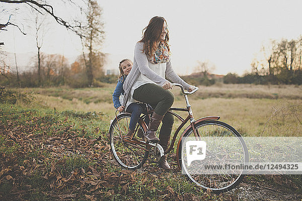 A mother pedals an old fashioned bike while her daught rides on the back.