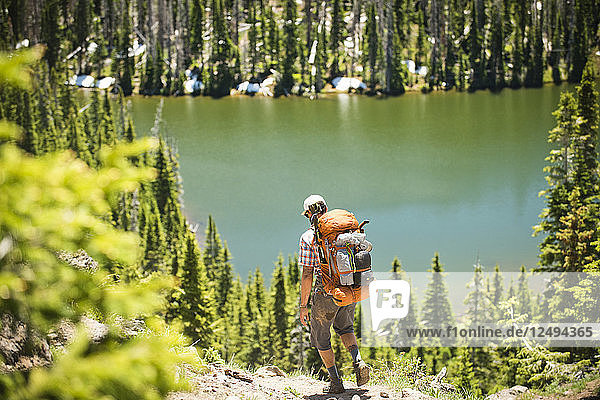 Ein Rucksacktourist wandert auf einem Pfad mit einem Bergsee in der Ferne.