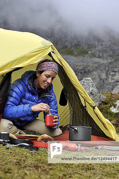 Woman hiker prepares a meal at camp during a backpacking trip to Reed Lakes in the Talkeetna Mountains near Palmer  Alaska August 2011.