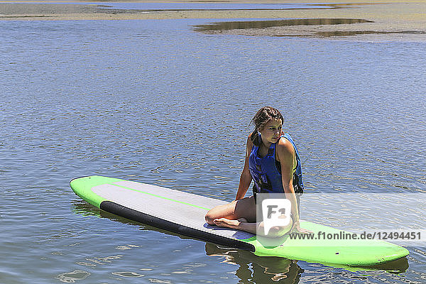 A Teenage Girl Sitting On A Paddleboard In Calm Lake