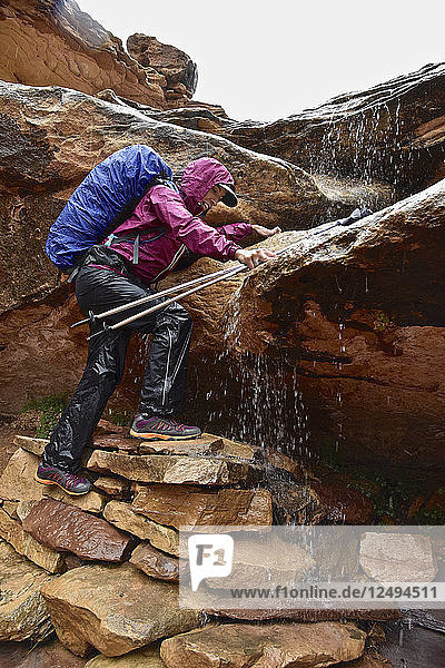 Frau klettert auf Felsen und navigiert durch einen Wasserfall im Canyonlands National Park