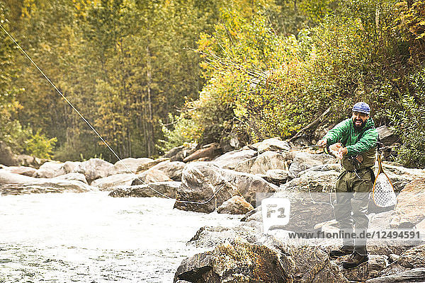 A fly fisherman in a river surrounded by fall foliage in Revelstoke  British Columbia.