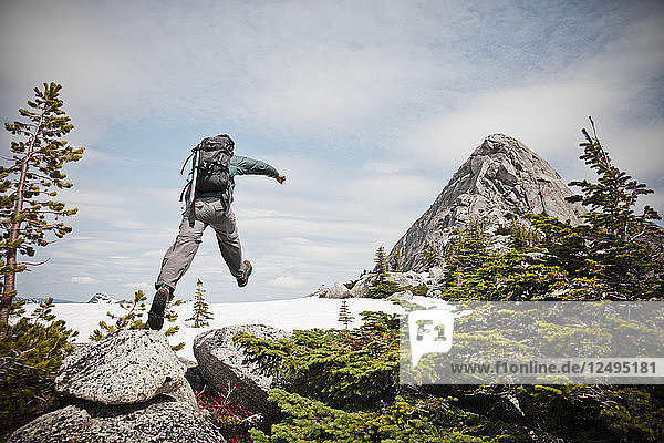 Ein Rucksacktourist springt auf ein Stück Schnee  während er sich dem Gipfel des Needle Peak nähert.