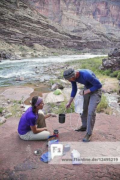 Hikers cook dinner on a cliff-pinched patio above camp and the Colorado River near Deer Creek Falls in the Grand Canyon outside of Fredonia  Arizona November 2011. The 21.4-mile loop starts at the Bill Hall trailhead on the North Rim and descends 2000-feet in 2.5-miles through Coconino Sandstone to the level Esplanada then descends further into the lower canyon through a break in the 400-foot-tall Redwall to access Surprise Valley. Hikers connect Thunder River and Tapeats Creek to a route along the Colorado River and climb out Deer Creek.