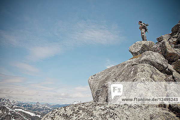 A hiker stands on a pile of granite rock near the summit of Needle Peak.