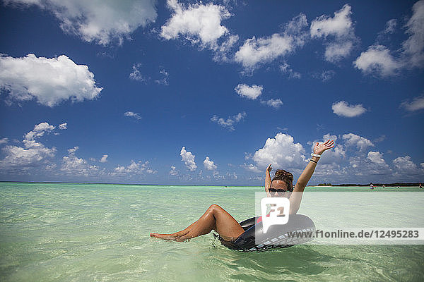Eine junge Frau im Bikini schwimmt während ihres Urlaubs in Cayo Coco  Kuba  auf einem aufblasbaren Schlauch im türkisfarbenen Wasser.