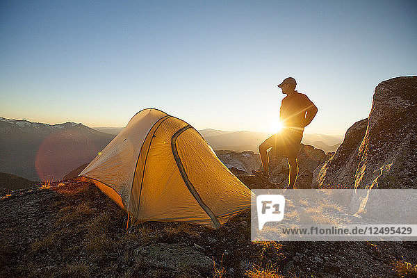 A silhouetted hiker partially blocks he sunset while camping on Saxifrage Peak  Pemberton  BC  Canada.