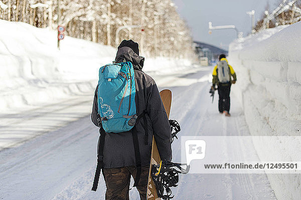Snowboarders Walking Along Snow Covered Side Walk To Resort In Niseko  Japan