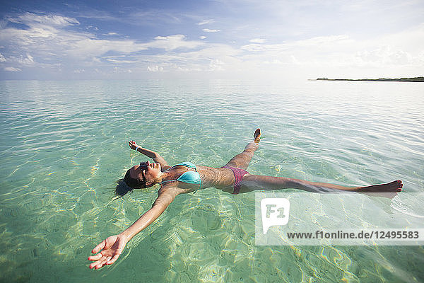 Eine junge Frau schwimmt im Urlaub in Cayo Coco  Kuba  auf dem Rücken mit ausgestreckten Gliedmaßen im seichten türkisfarbenen Wasser.