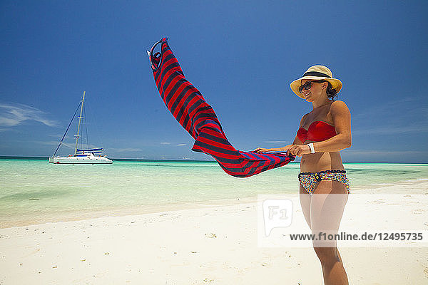 Eine junge Frau im Bikini schüttelt den Sand von ihrem Sommerkleid  während sie einen schönen Strand in Kuba genießt.