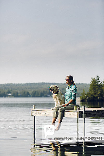 Woman And Dog Sitting On The Edge Of Dock On Caspian Lake