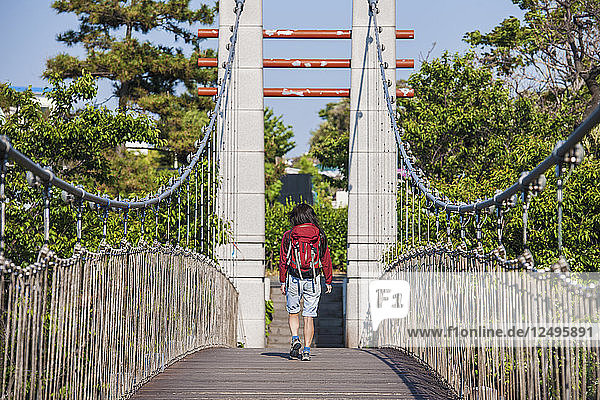 Frau geht über eine Hängebrücke über den Fluss Yongyeon in Jeju Si auf der Insel Jeju