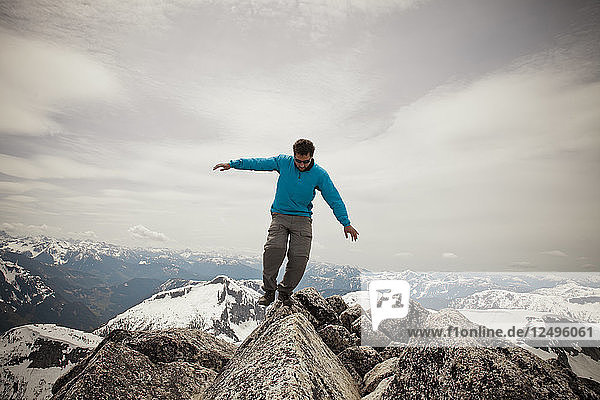 A hiker balances on a granite rock on the summit of Needle Peak.