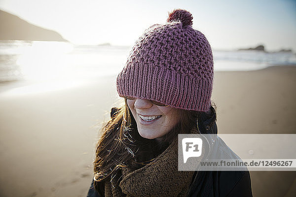 Eine Frau trägt eine Haube über ihrer Brille  während sie am Strand spazieren geht.