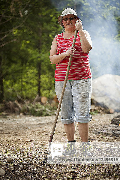 Porträt einer Frau mittleren Alters  die eine Gartenharke hält.