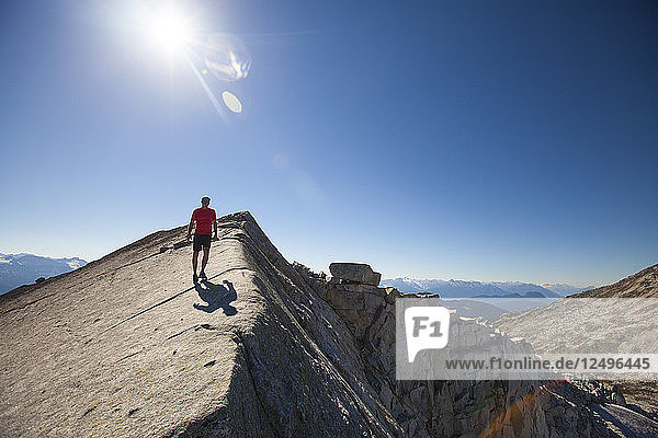 A hiker walks across a rocky slab ridge near the summit of Cassiope Peak  Pemberton  British Columbia  Canada.