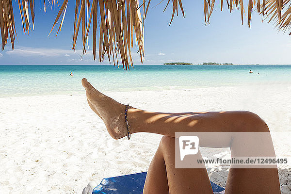 Beine eines Mädchens im Schatten einer Palme an einem Strand in Kuba