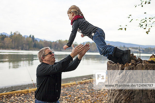 Ein älterer Mann fängt seine Enkelin auf  als sie von einem Baumstumpf springt