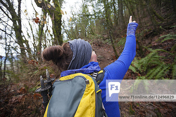 Eine junge  aktive Frau zeigt auf einige Wildtiere  während sie mit dem Rucksack durch einen dichten Wald wandert.