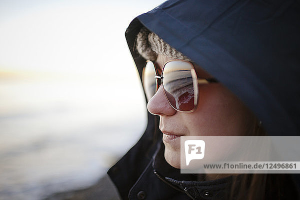 Portrait of a young woman wearing sunglasses and a hooded jacket while at White Rock Beach  British Columbia  Canada.