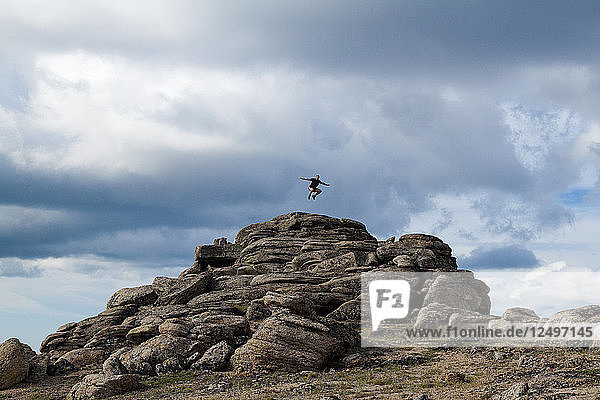 A backpacker jumps into the air off a rocky formation in Cliff City  a area with unique geology in Cathedral Lakes Provincial Park  British Columbia  Canada.