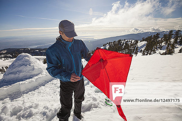 A Hiker Preparing To Fly A Kite On The Top Of A Snow Covered Mountain