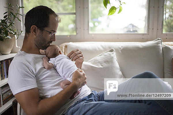Ein Vater hält sein Baby im Arm  während er zu Hause sitzt