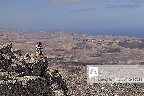 Mädchen sitzt auf dem Gipfel eines Berges mit einer schönen Wüste und trockenen Landschaft unter ihr fotografieren.