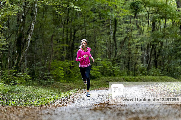Frau mit rosa Oberteil  die allein auf einer Straße in einem grünen Wald im Herbst läuft  in der Nähe von Eloise  Frankreich